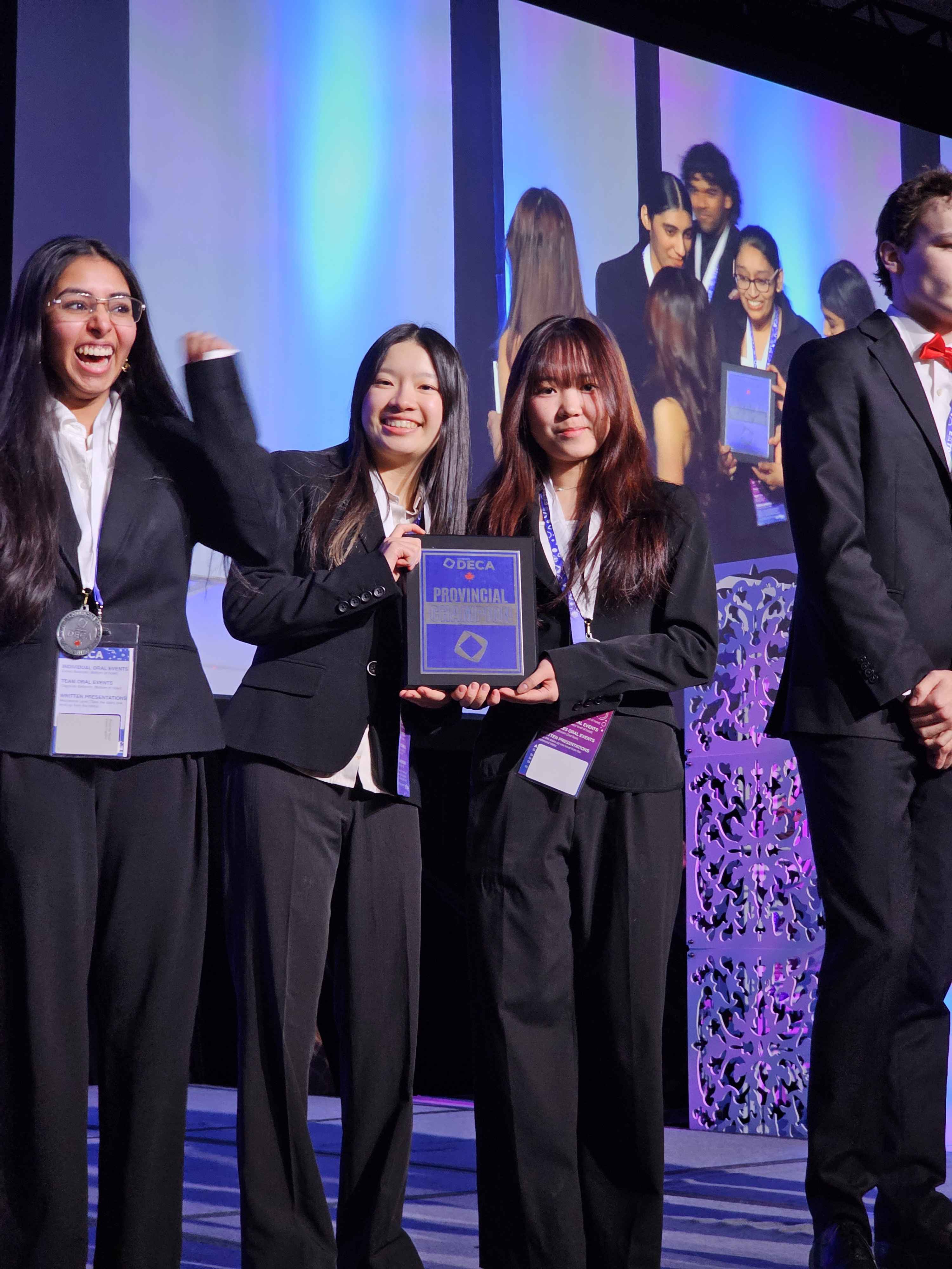 Students on stage holding a DECA provincial plaque during an awards moment.